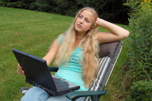 A young caucasian woman outdoors in a meadow, working on her computer